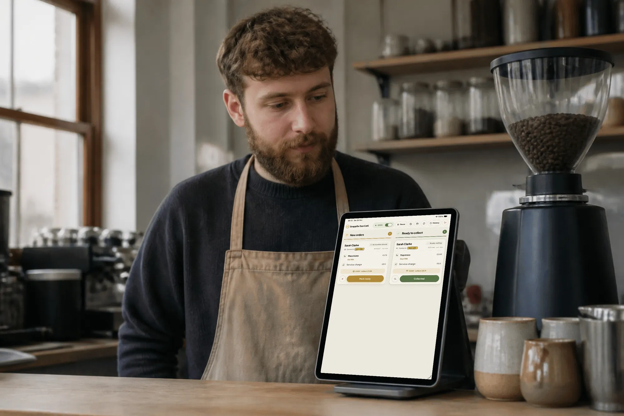 A barista at the counter with an upright tablet showing the SnappGo order board